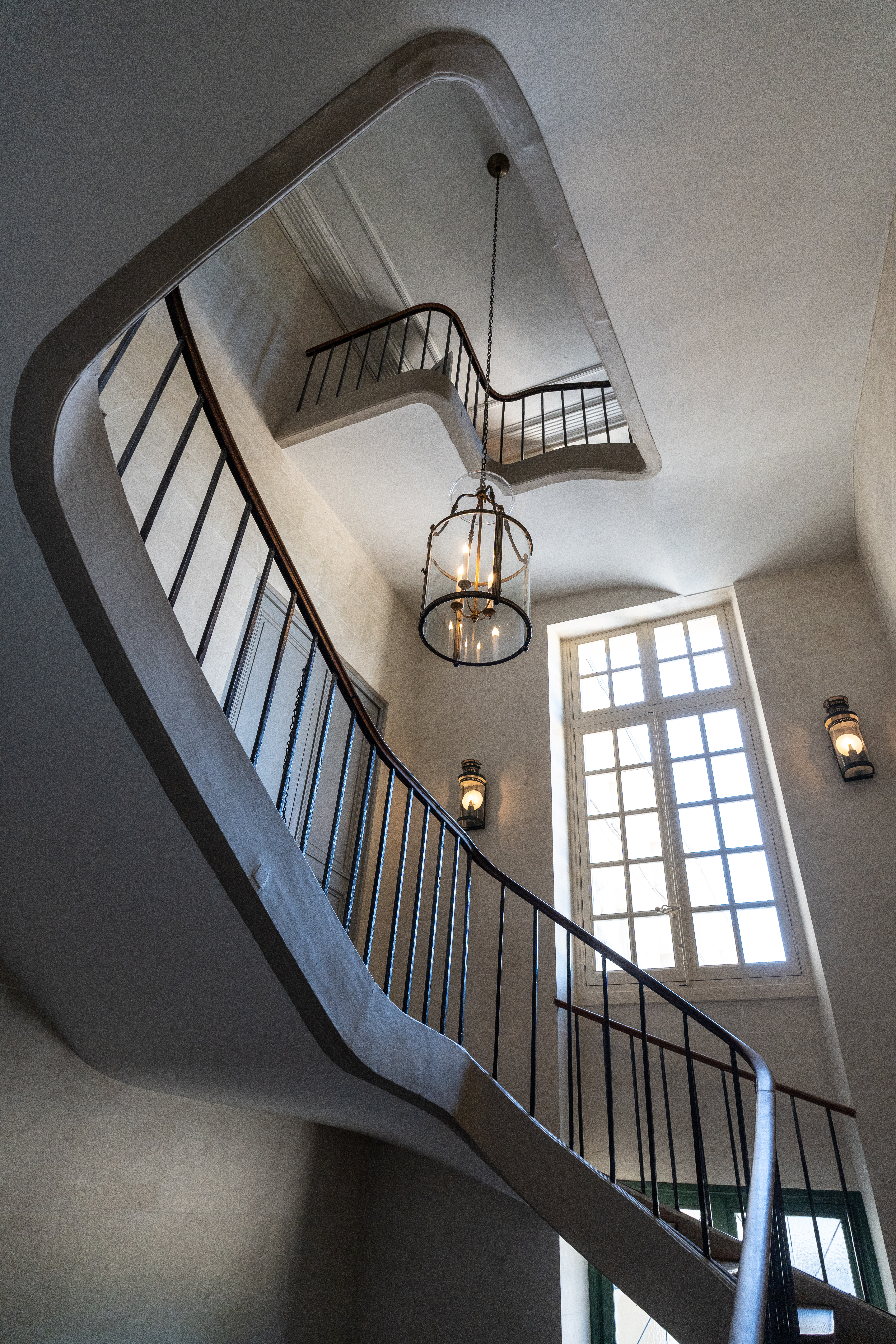 Vue des escaliers de l'aile sud en contre-plongée avec un lustre au centre 