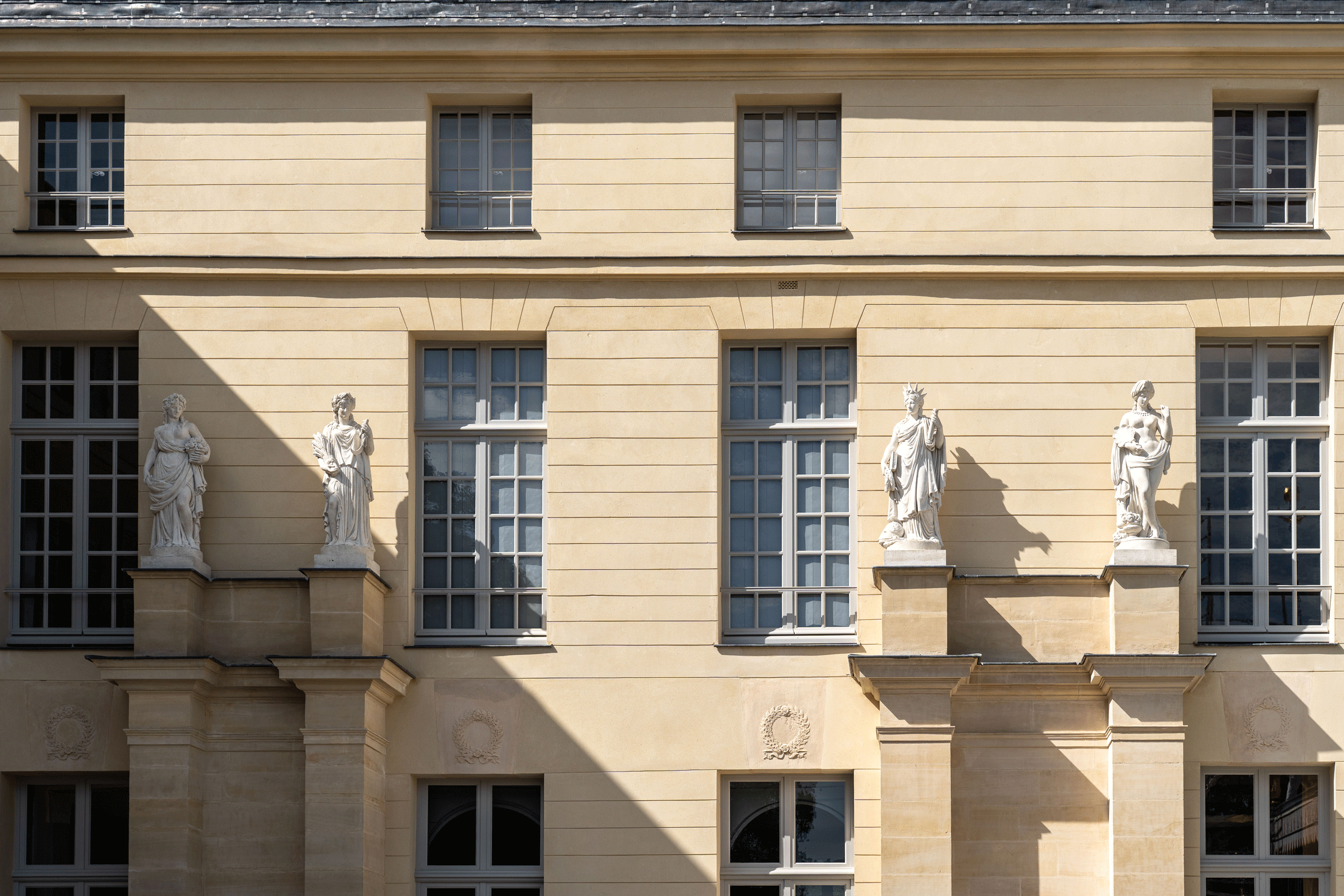 Quatre statues alignées, éclairées par le soleil avec leurs ombres portées sur la pierre