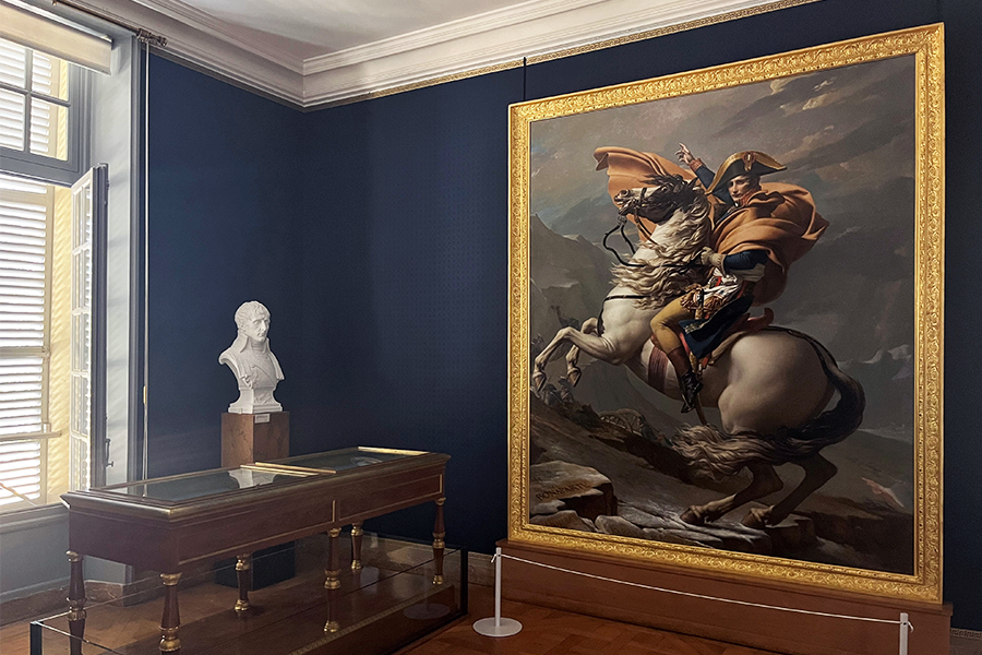 Grand tableau représentant Bonaparte à cheval accroché à un mur, avec une vitrine en bois et un buste en marbre à proximité