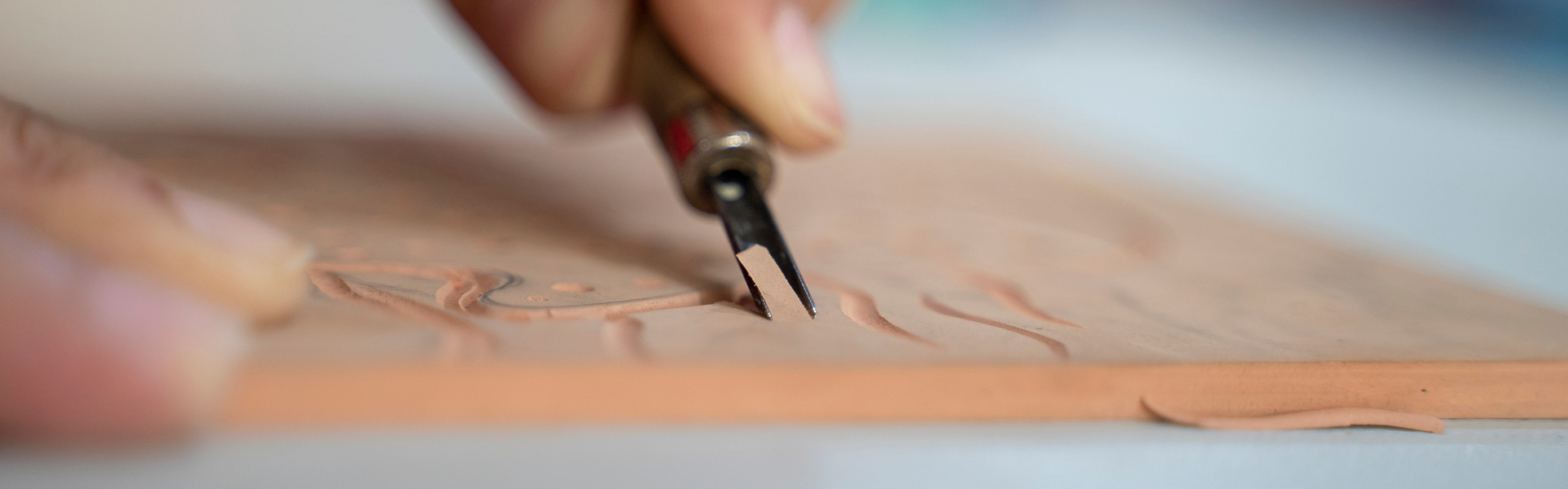 Détail d’une main maniant une gouge, réalisant des incisions précises sur une plaque de linoléum