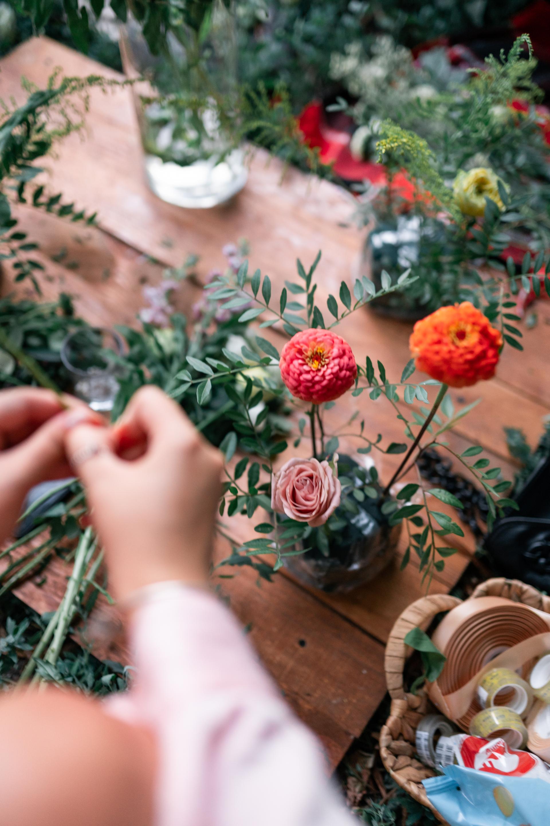 Mains travaillant à la réalisation d'un bouquet aux fleurs rouges, roses et orangées