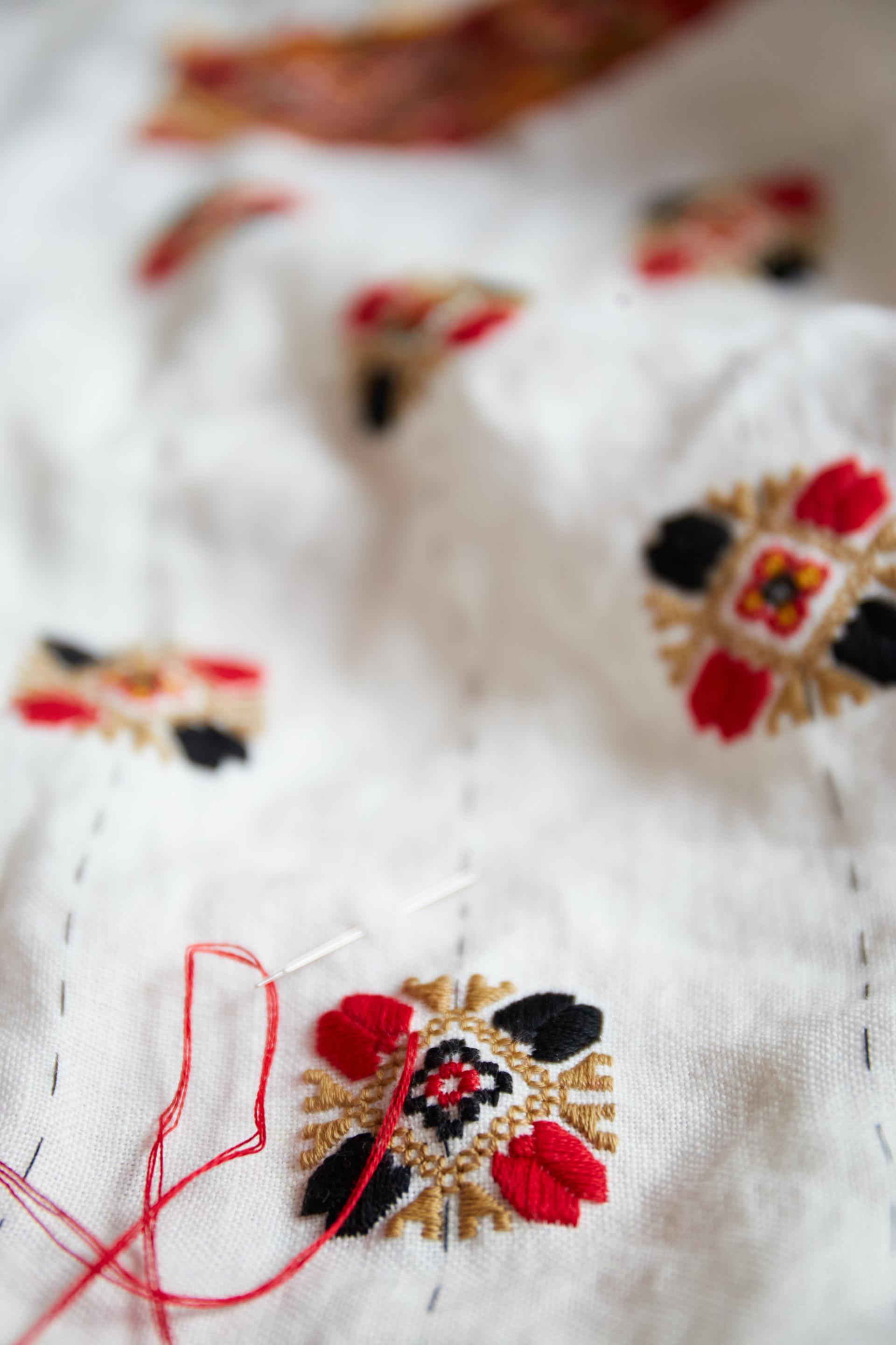 Détail d’un tissu blanc brodé, une aiguille traversant le motif avec un fil rouge visible