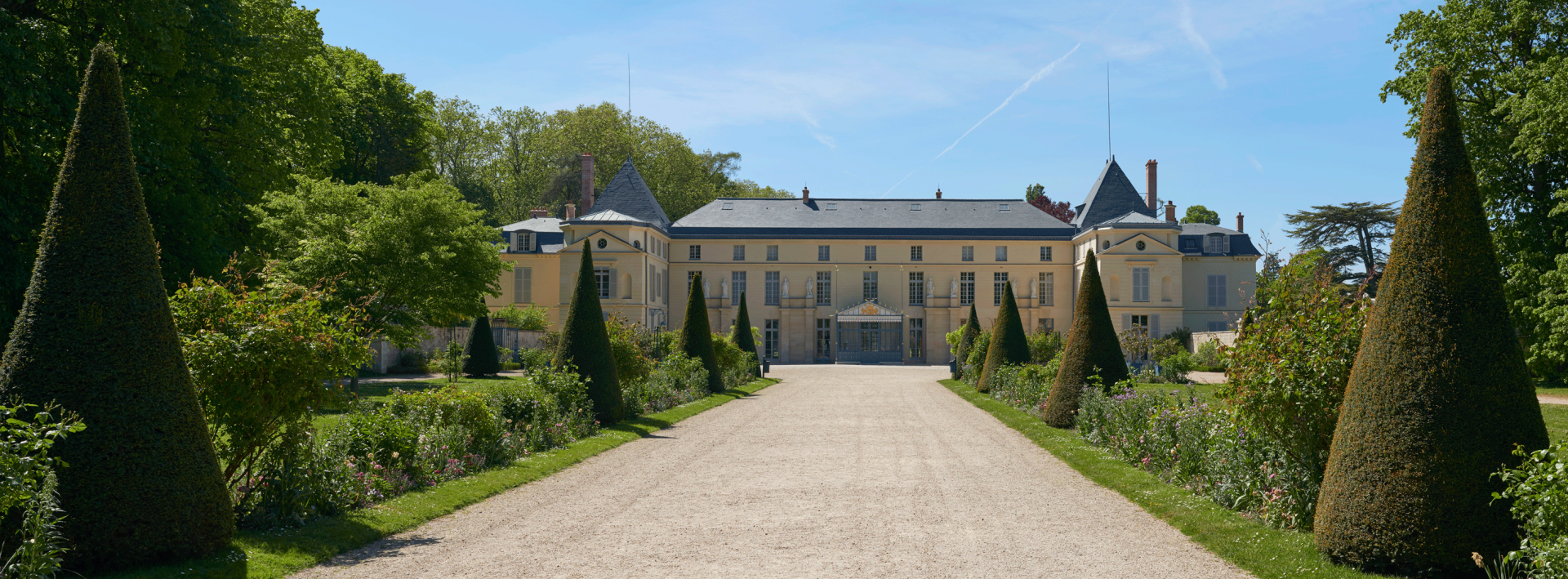 Chemin bordé d’ifs et de parterres fleuris menant au château de Malmaison.