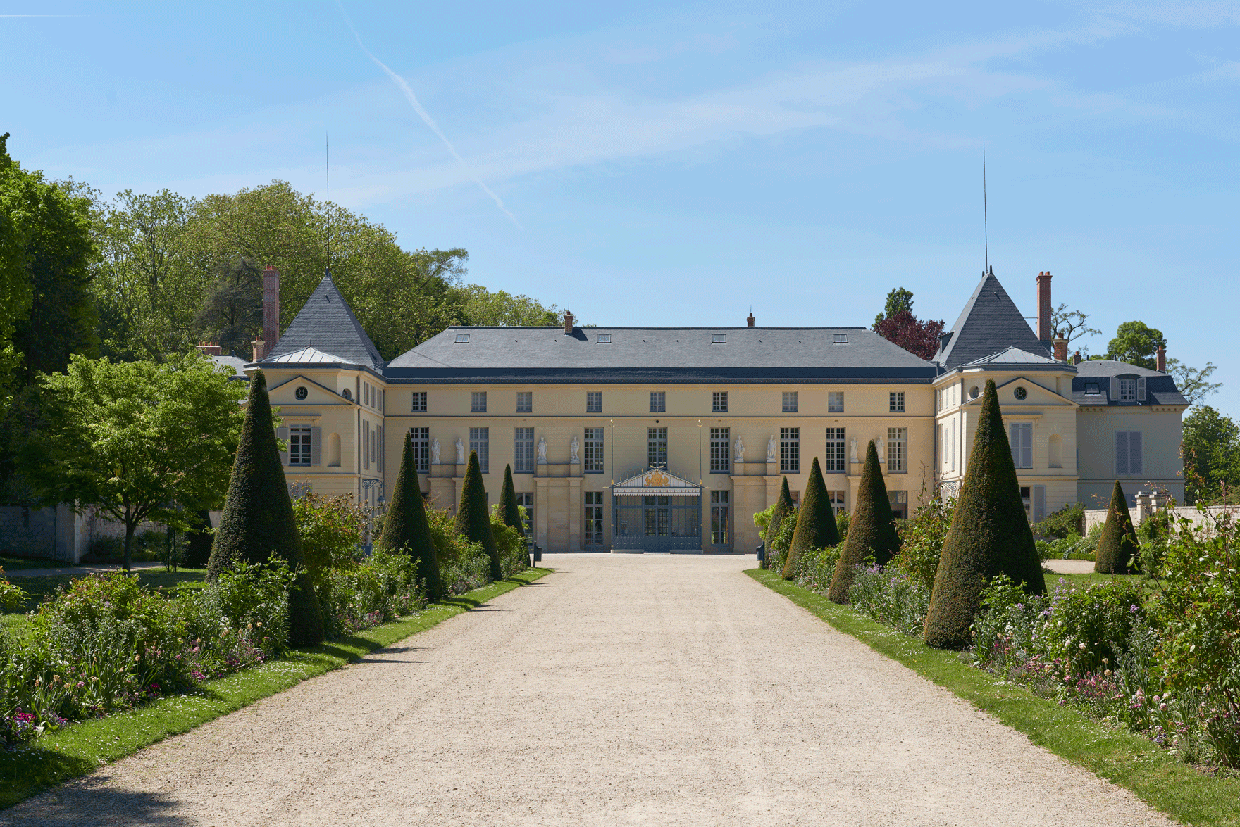 Chemin bordé d’ifs et de parterres fleuris menant au château de Malmaison.